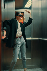 Stylish woman in black jacket and sunglasses posing in elevator, fashion model