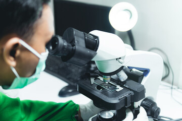 Scientist Looking Under Microscope, Wearing Green Protective Clothing. Hospital Medical Development...
