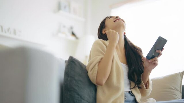 Happy young asian woman relax on comfortable couch at home texting messaging on smartphone, smiling girl use cellphone, chatting online message, shopping online from home