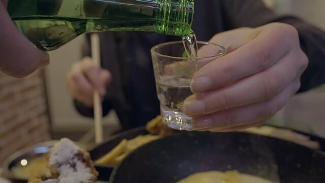 This POV video shows a soju sake bottle pouring alcohol into a shot glass in slow motion.