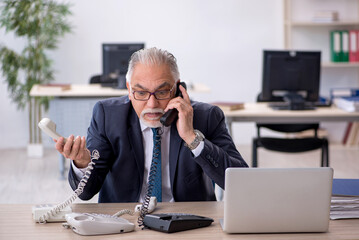 Old male employee speaking on the phone at workplace