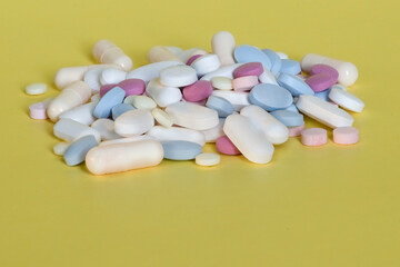 Closeup of a stack of pills, tablets and capsules on a yellow background with copy space on bottom.