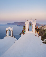 Men and women visit the whitewashed Greek village of Oia during a vacation in Santorini with blue...