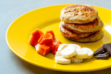 Pancakes on a yellow plate with fruits and chocolate.