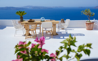 outside terrace of a restaurant by the ocean of Santorini Greece, chairs, and tables with flowers...