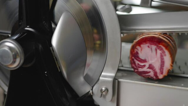 Prosciutto being sliced at an Italian deli. Fresh deli meat being sliced on a meat slicer.