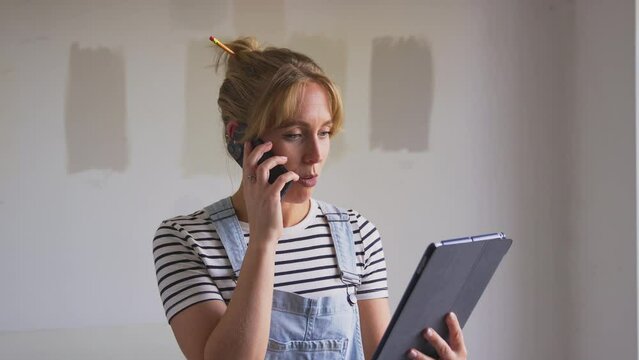 Woman decorating room in house making phone call looking at digital tablet with paint test strips in background - shot in slow motion