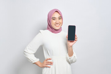 Smiling young Asian Muslim woman showing mobile phone blank screen, recommending new App isolated over white background