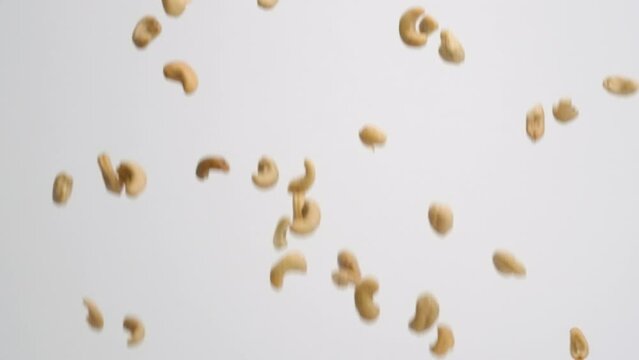 Whole roasted and salted cashew nuts raining down and bouncing back into frame on white backdrop in slow motion