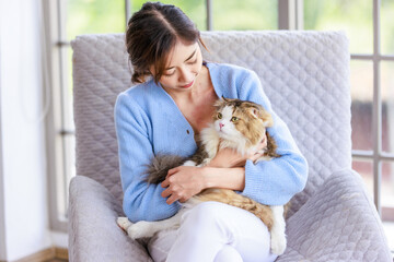 Millennial Asian young female owner sitting on cozy armchair smiling holding hugging cuddling...