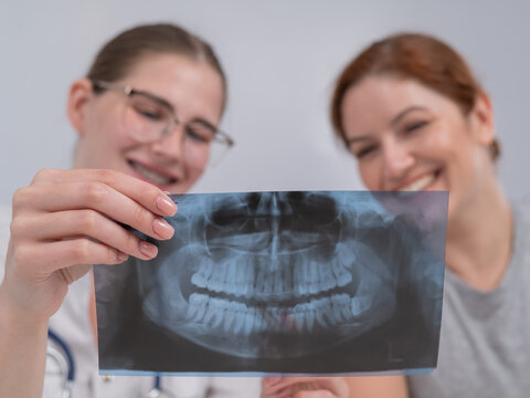 A woman doctor and a patient at the reception are discussing an x-ray of the jaw.