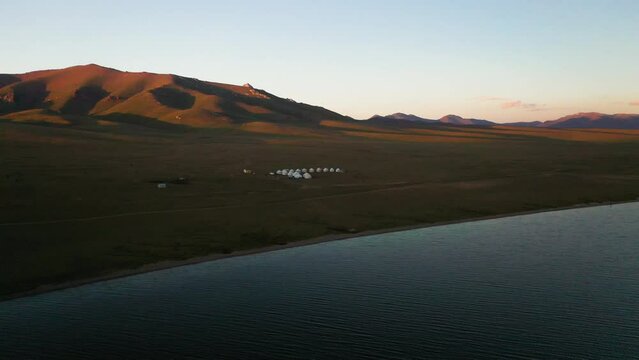 Rotating revealing drone shot of the small yurt village and the surrounding mountains beside the Song-Kol lake in Kyrgyzstan, sun setting