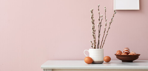 Pussy willow branches and Easter eggs on table near pink wall