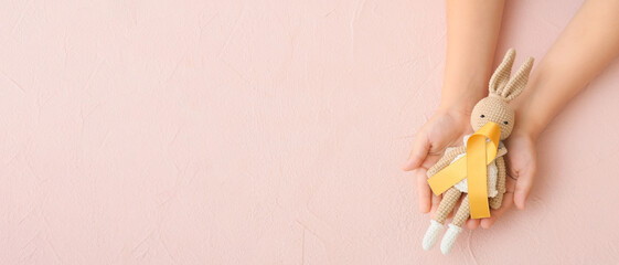Hands with toy and golden ribbon on beige background with space for text. Childhood cancer...