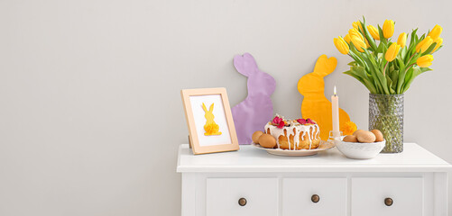 Easter cake, eggs and decorations on table near light wall in room