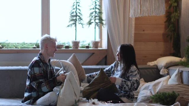 Happy young beauty couple in love having Pillow Fight on sofa couch, enjoying funny leisure activity together at home