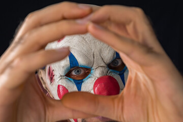 The face of a man wearing a scary clone mask through clenched palms. Close-up. The creepy clown...
