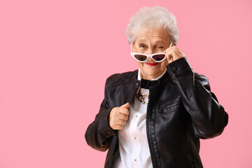 Senior woman in sunglasses winking on pink background