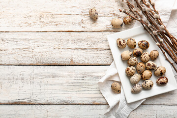 Plate with Easter eggs and willow branches on light wooden background