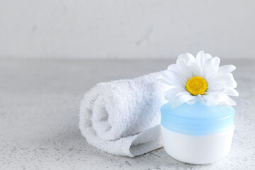 Obraz na płótnie Canvas Jar of cosmetic product, towel and chamomile flower on light background