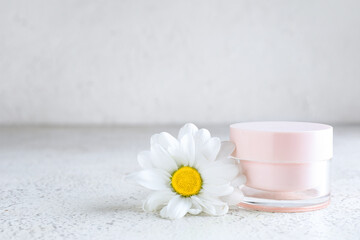 Jar of cosmetic product and chamomile flower on light background