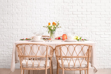 Table setting for International Women's Day celebration and vase with flowers in dining room near white brick wall