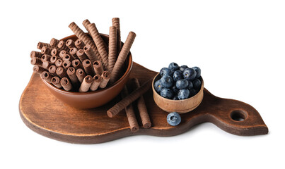 Board with bowl of delicious chocolate wafer rolls and blueberries isolated on white background