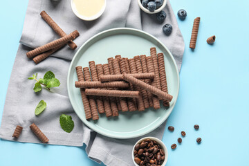 Composition with delicious chocolate wafer rolls, blueberries, coffee beans, condensed milk and mint on blue background