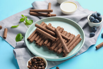 Composition with delicious chocolate wafer rolls, blueberries, coffee beans, condensed milk and mint on blue background