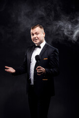 Stylish young man holding microphone, posing on dark background, actor, singer, show, host of event