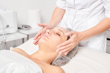 Beautician rubbing moisturizing cream mask into woman face skin for rejuvenation, anti aging...