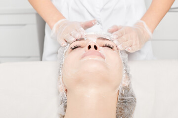 Cosmetologist massages cream mask into woman face skin for rejuvenation, anti aging skincare...