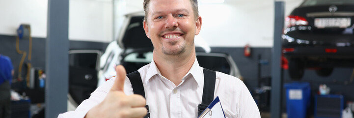 Happy smiling auto mechanic showing thumbs up gesture in workshop