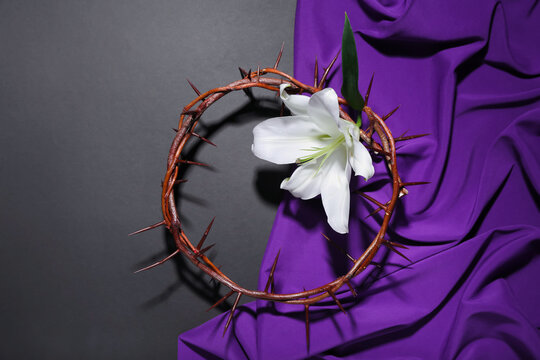 Crown of thorns with lily flower and purple fabric on dark background. Good Friday concept