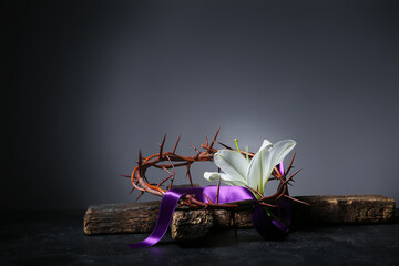 Crown of thorns with lily, purple ribbon and cross on dark background. Good Friday concept