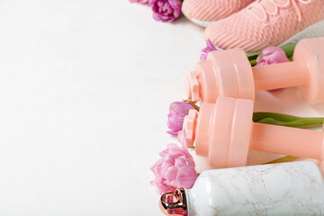 Dumbbells with sports water bottle and tulips on white background, closeup. Hello spring