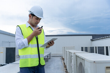Asian maintenance engineer works on the roof of factory. contractor inspect compressor system and plans installation of air condition systems in construction. technology, online checking, mobile