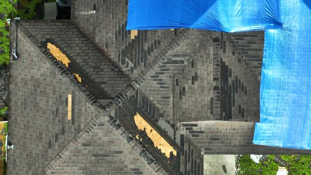 Top view of leaking house roof covered with protective tarp sheets against rain water leaks until replacement of asphalt shingles.