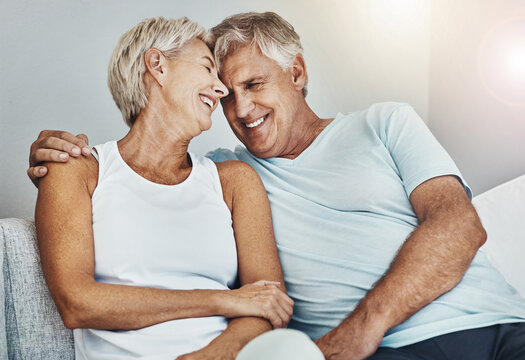 Love, Laughing And Retirement With A Senior Couple Sitting In The Living Room Of Their Home Together. Happy, Smile Or Relax With A Mature Man And Woman Joking While Bonding On The Couch In A House