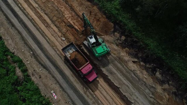 Top-down aerial view of truck and bulldozer loading and unloading soil at the road construction site