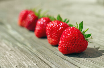 Row of ripe strawberry berries on old wood desk, selective focus. Harvested red berries on wooden background closeup.