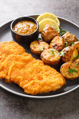 Munchner Schnitzel with baked potatoes and Dijon mustard closeup on the plate on the table. Vertical