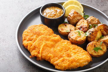 Delicious German Munich schnitzel fried breaded with mustard and horseradish served with baked potatoes close-up in a plate on the table. horizontal