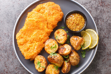 Delicious German Munich schnitzel fried breaded with mustard and horseradish served with baked potatoes close-up in a plate on the table. horizontal top view from above