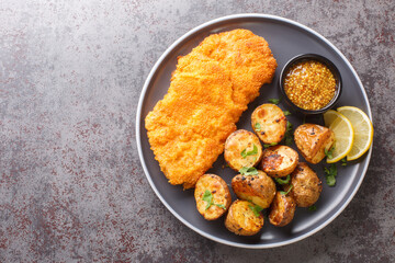 Homemade Munich veal schnitzel fried in breadcrumbs with mustard and horseradish garnished with baked potatoes close-up in a plate on the table. horizontal top view from above