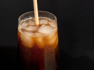 Glass of cola with ice on a black background. Close-up.