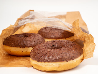 Chocolate donut with chocolate chips in a paper bag on a white background. close-up.