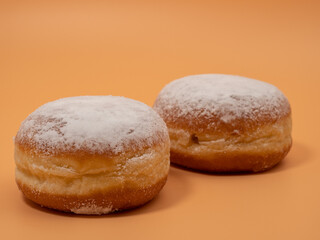 Freshly baked and dusted with powdered sugar German donuts. Donut berliner or krapfen on orange background.