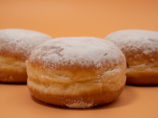 Freshly baked and dusted with powdered sugar German donuts. Donut berliner or krapfen on orange background.