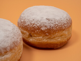 Freshly baked and dusted with powdered sugar German donuts. Donut berliner or krapfen on orange background.